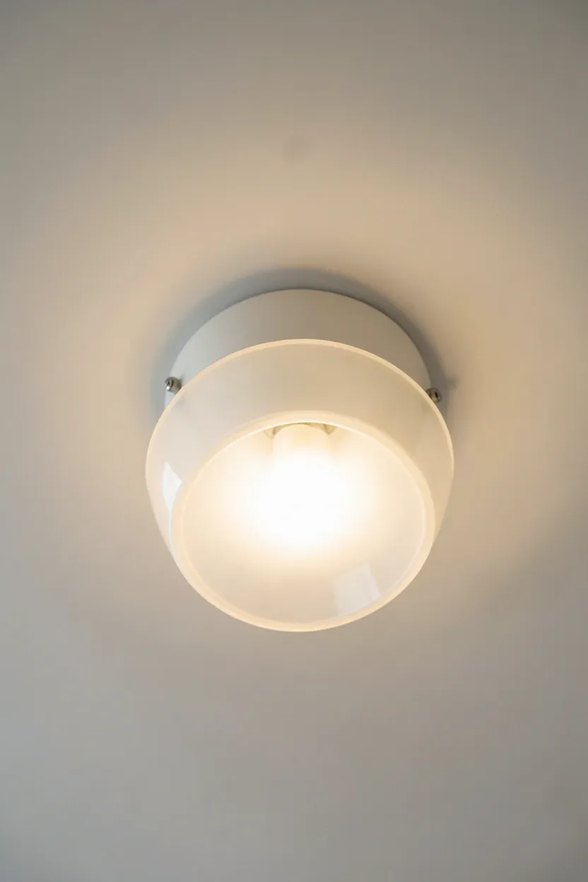 Frosted glass ceiling light fixture diffusing warm ambient glow in a neutral bedroom with cream walls