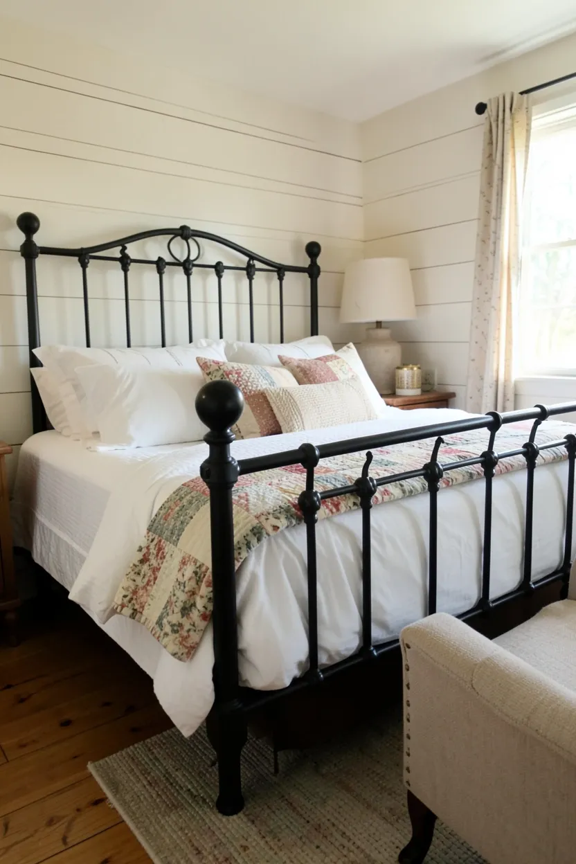 Vintage matte black wrought iron bed with white quilted bedding against a shiplap wall in a cozy farmhouse bedroom