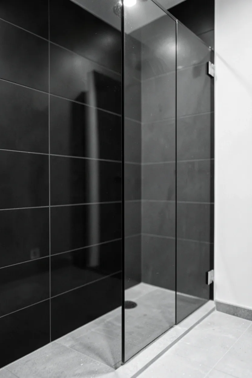 Black glass mosaic shower tiles on wall reflecting light in a modern bathroom — sleek wet area with light-colored stone floor