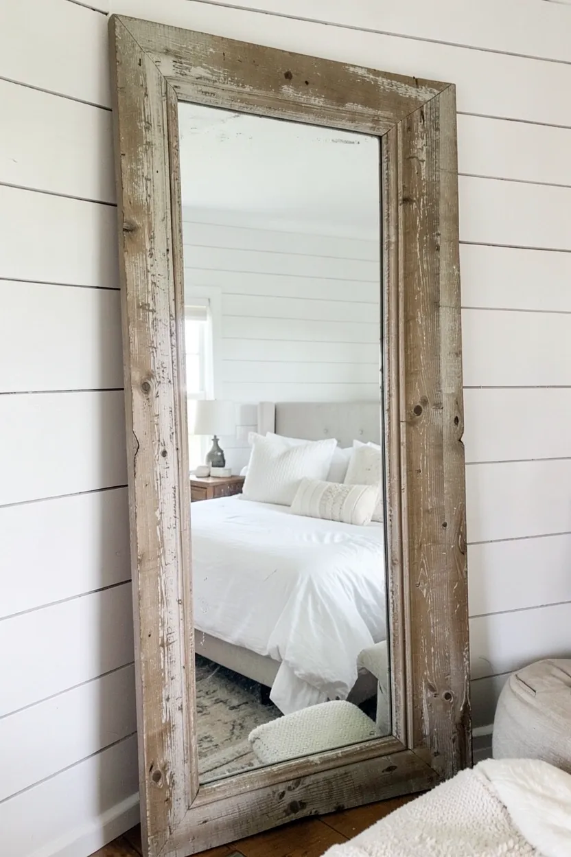 Large floor mirror with distressed wood frame leaning against a neutral wall in a vintage farmhouse bedroom